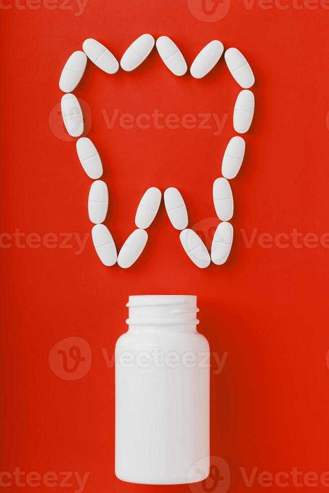 Calcium vitamin in the form of a tooth spilled out of a white jar on a red background. photo