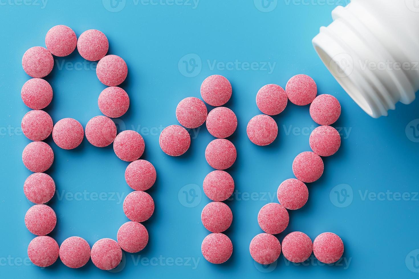 Pink pills in the shape of the letter B12 on a blue background, spilled out of a white can. photo