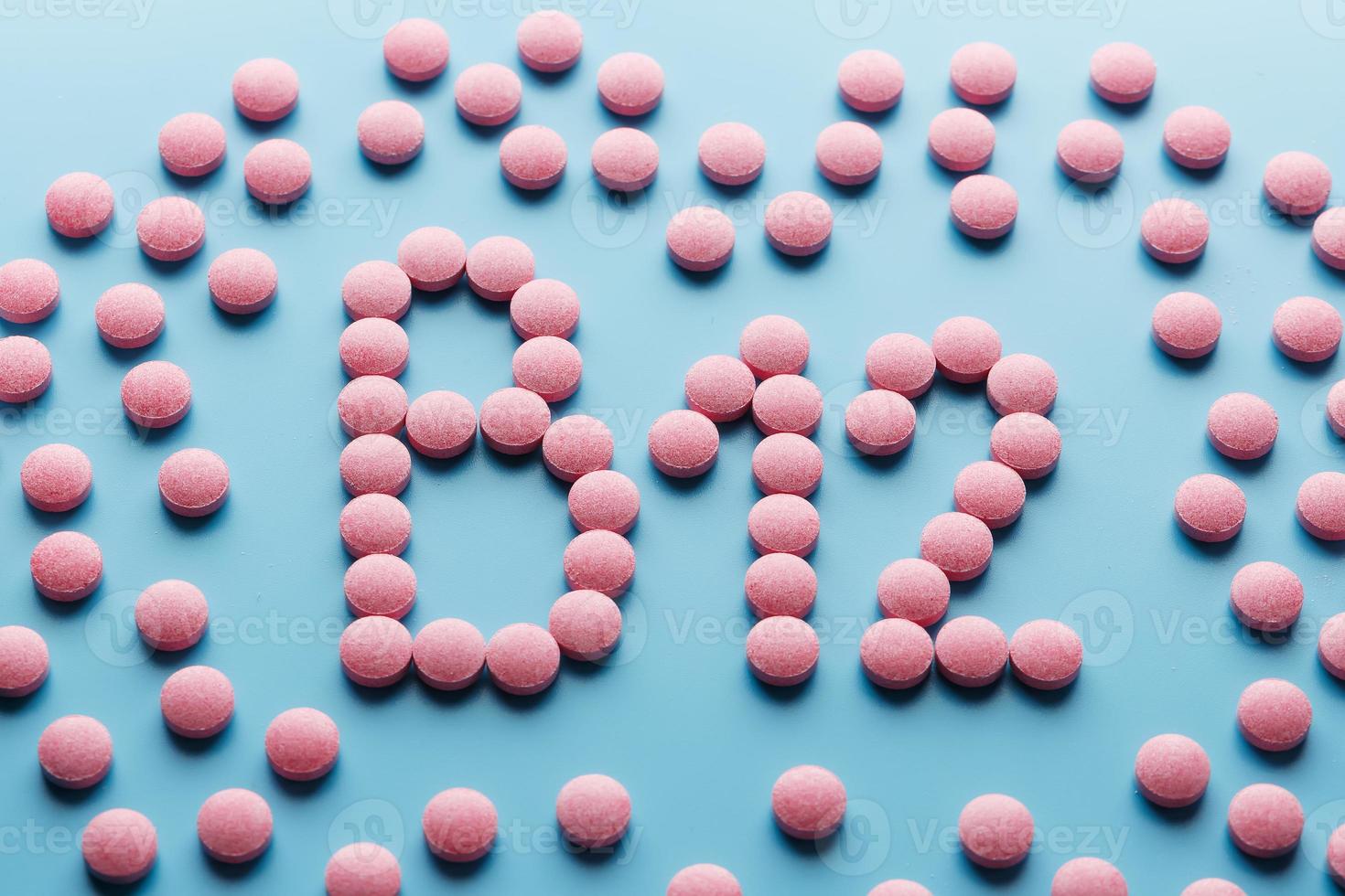 Pink pills in the shape of the letter B12 on a blue background, spilled out of a white can. photo