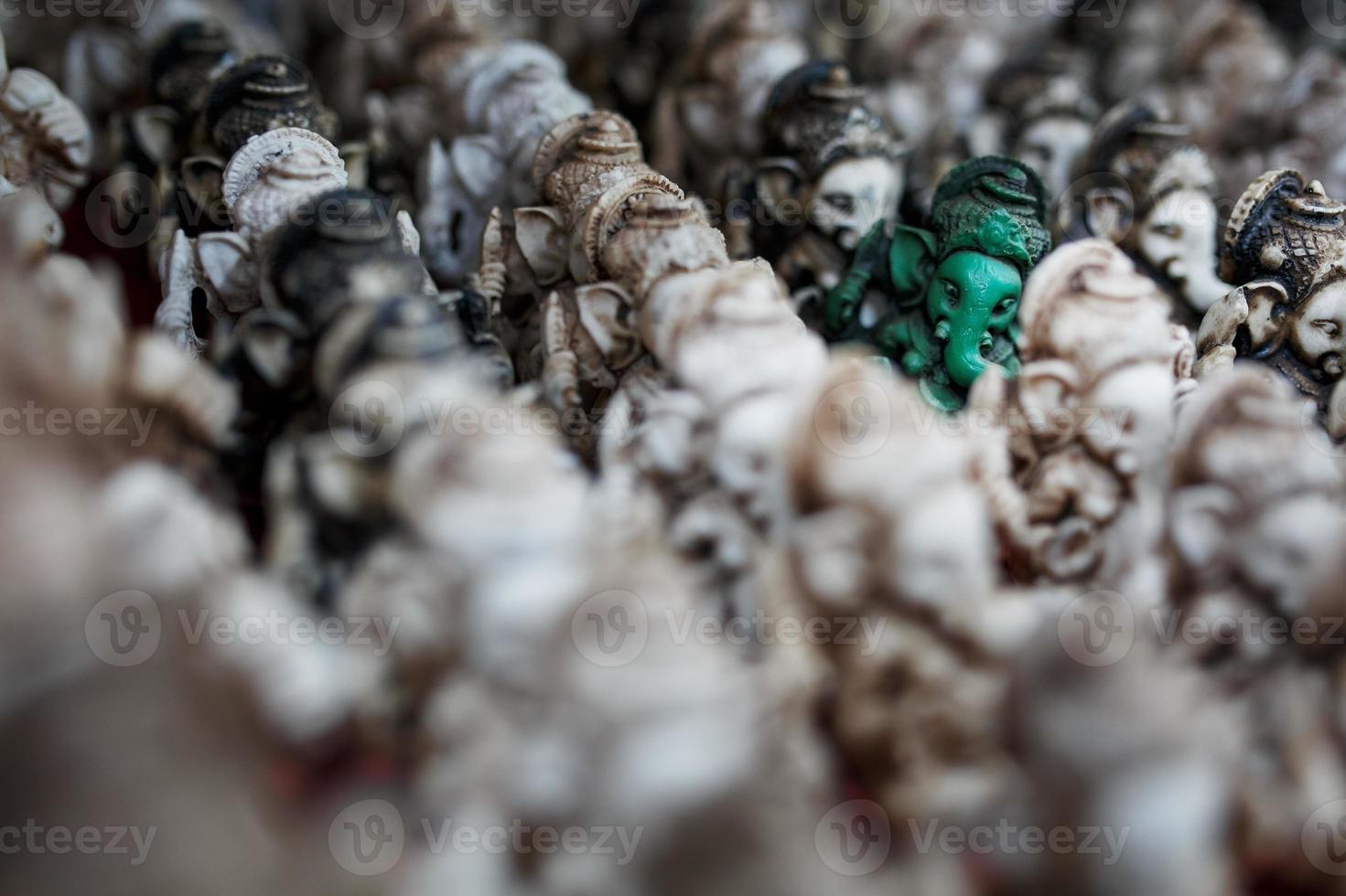 The stone statuette of Ganesh is green, contrasting with the group of light Ganesh on the counter of the Indian market photo