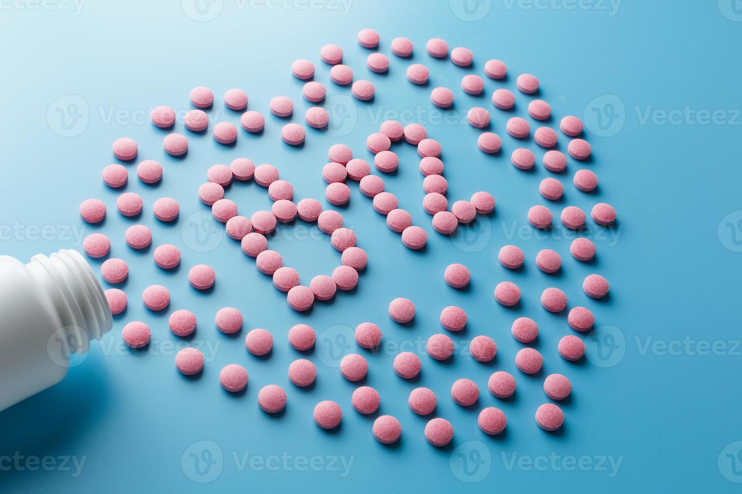 Pink tablets in the form of B12 in the heart on a blue background, spilled from a white can. photo