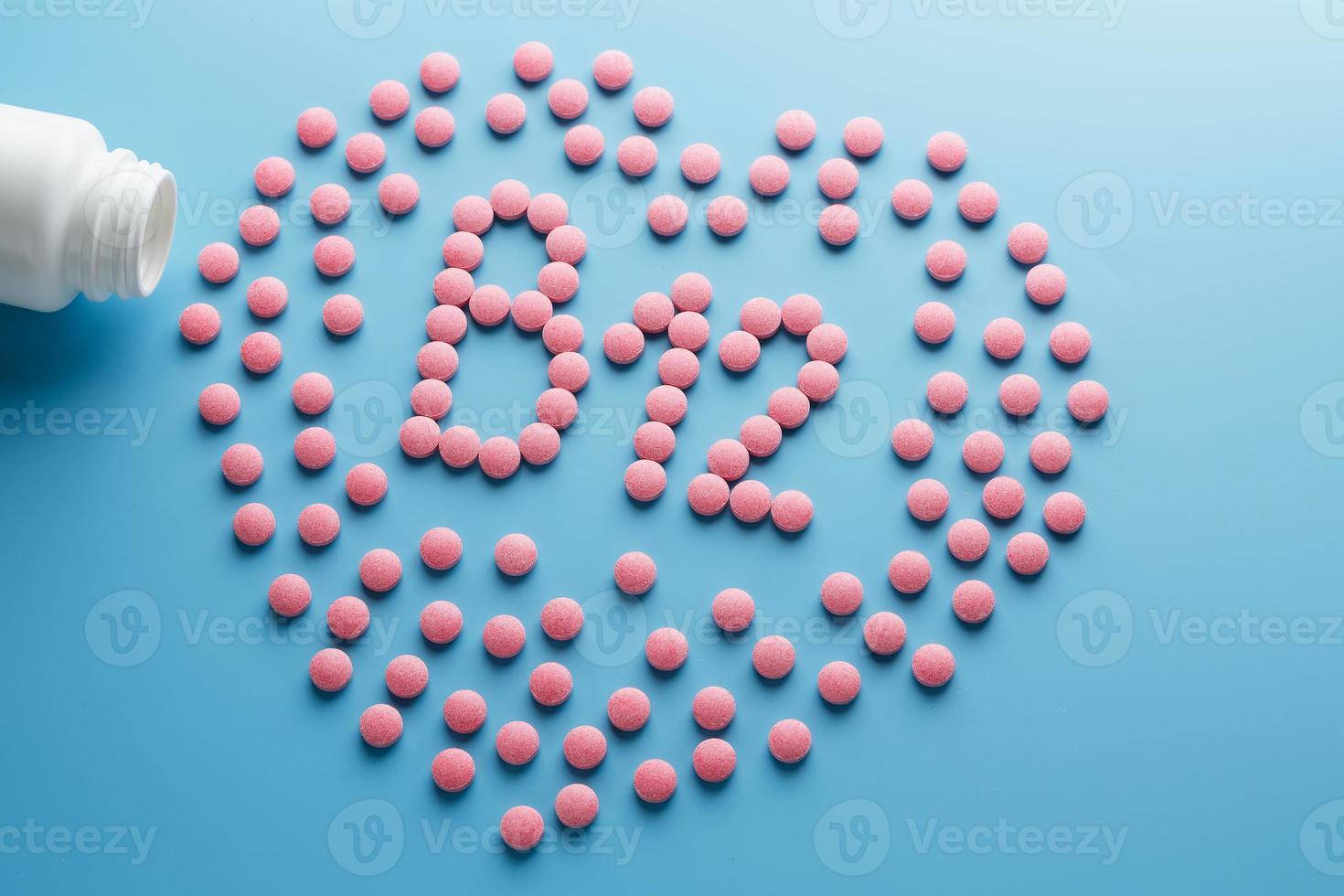 Pink tablets in the form of B12 in the heart on a blue background, spilled from a white can. photo