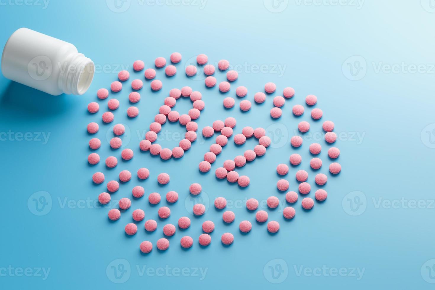 Pink tablets in the form of B12 in the heart on a blue background, spilled from a white can. photo