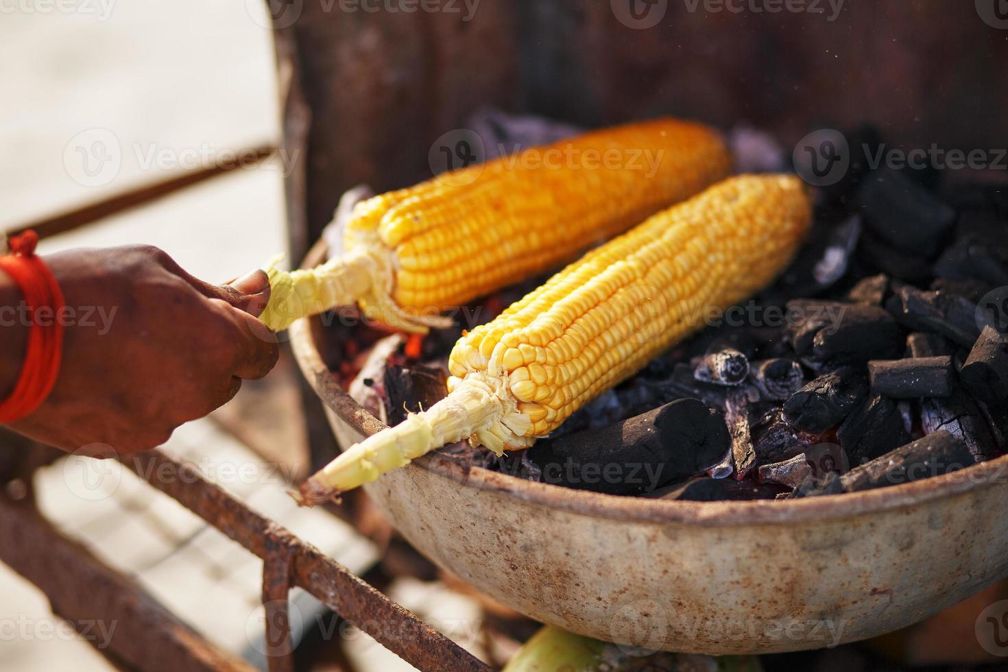 mazorcas de maíz a la parrilla. cerrar imagen con callos y manos. comida callejera asiática, india y china. playa de comida al atardecer de goa foto