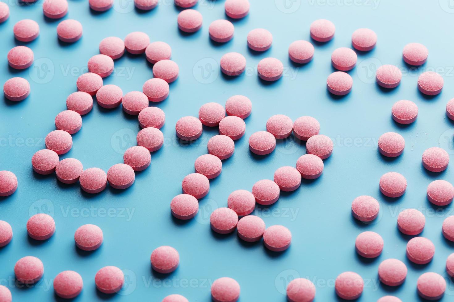 Pink pills in the shape of the letter B12 on a blue background, spilled out of a white can. photo