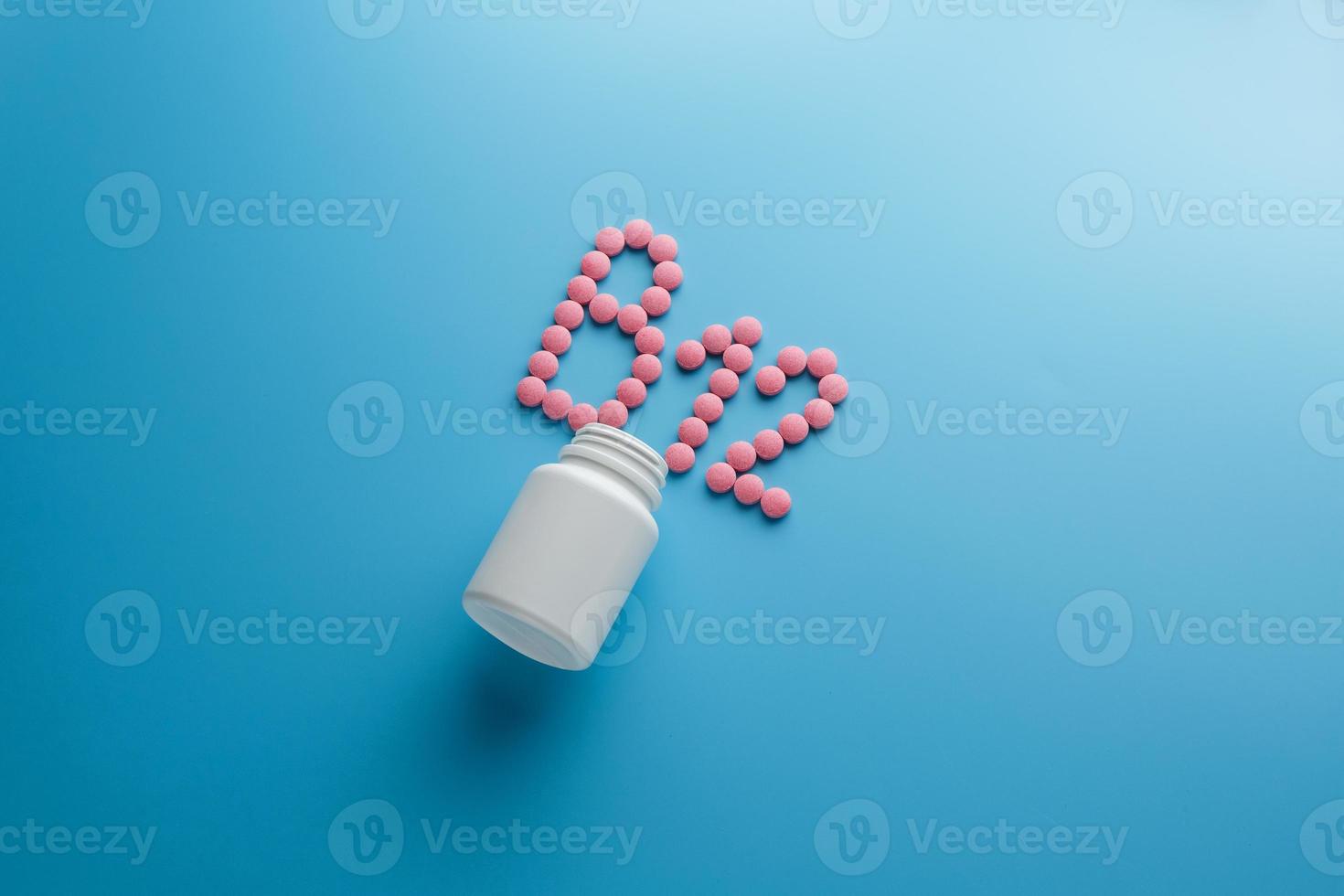 Pink pills in the shape of the letter B12 on a blue background, spilled out of a white can. photo