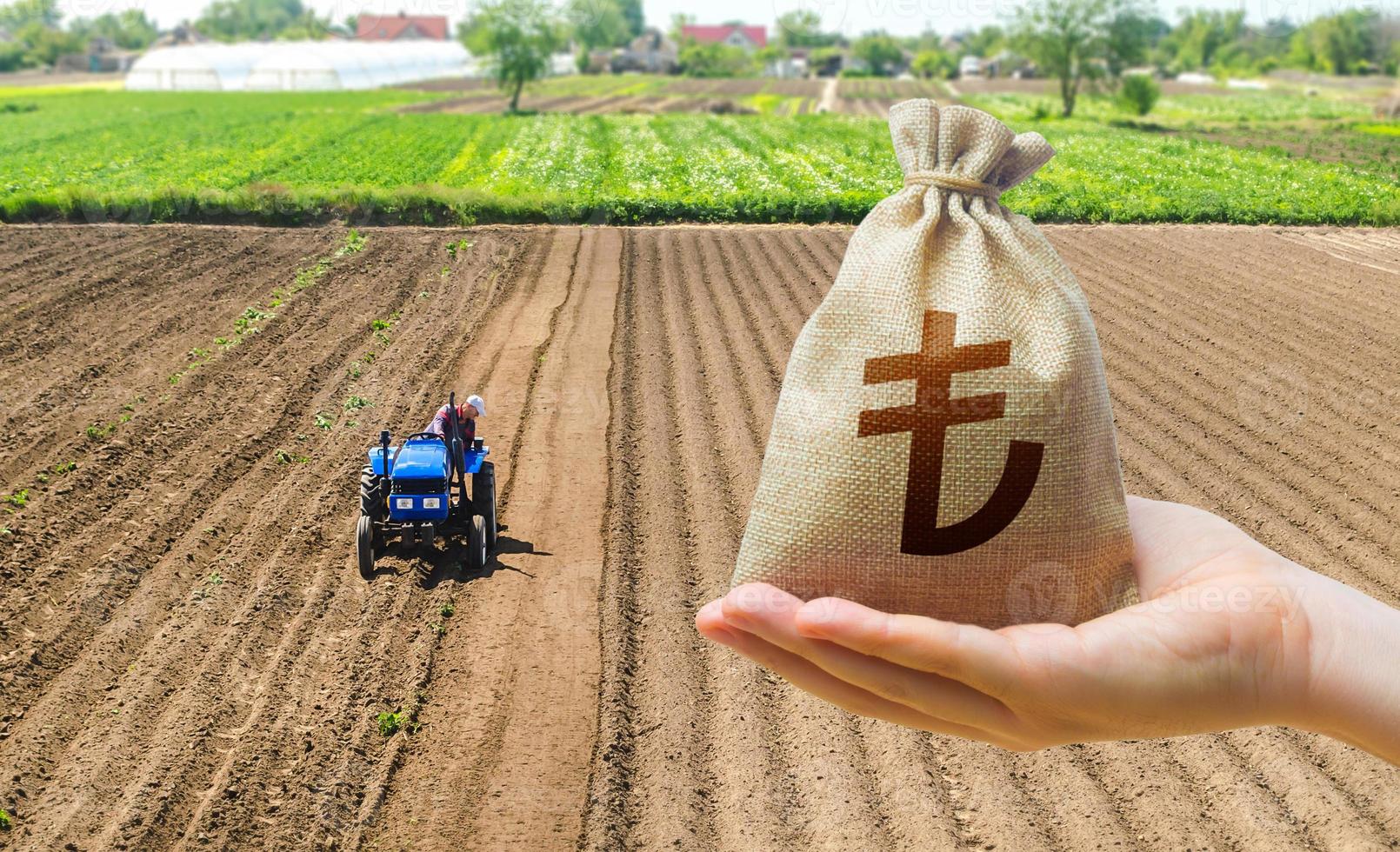 Hand with a Turkish lira money bag on the background of a farm field with a tractor. Subsidies support for agricultural producers. Land lease, land market. Investments in agriculture and agribusiness. photo