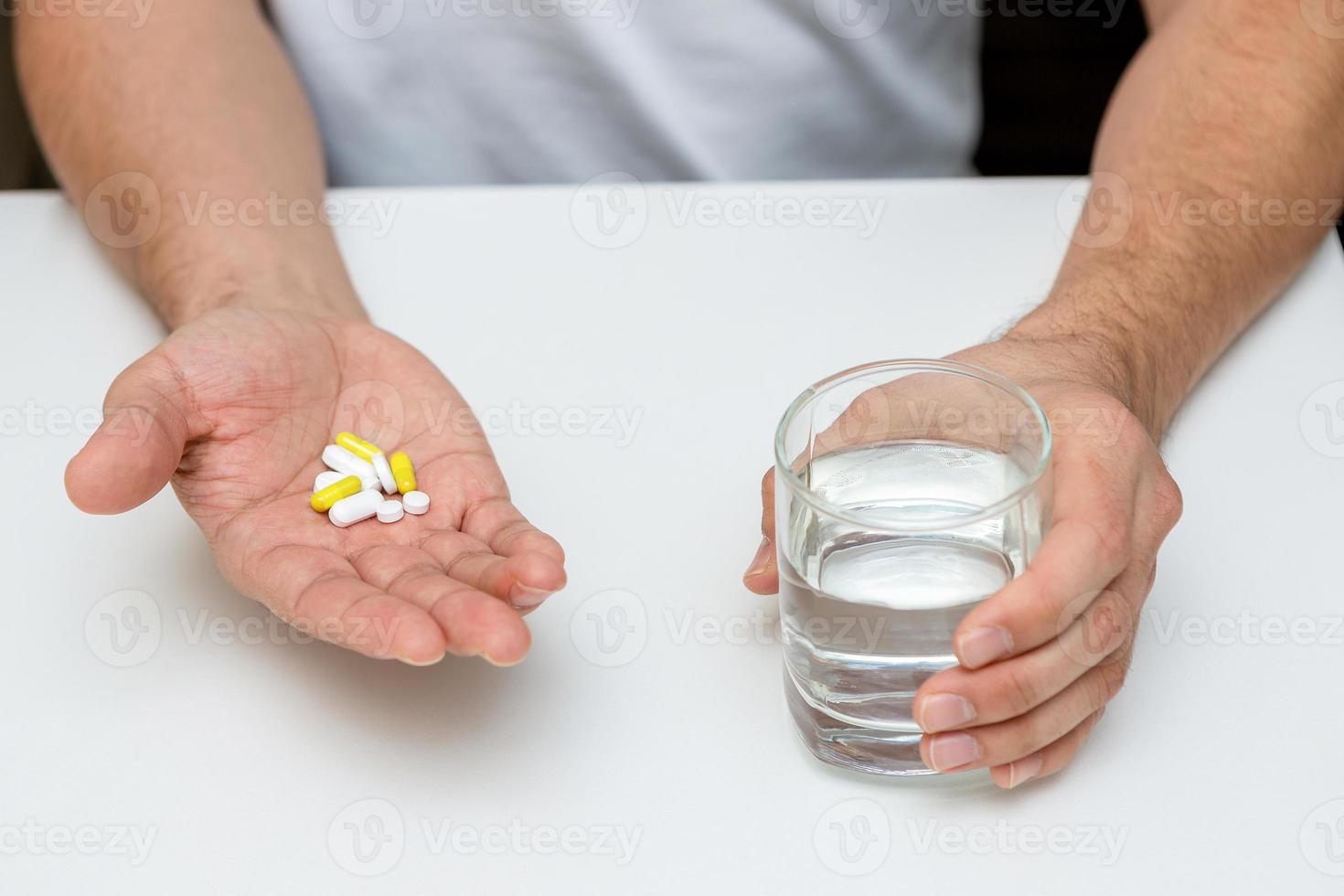 tabletas amarillas y un vaso de agua en manos de hombres foto