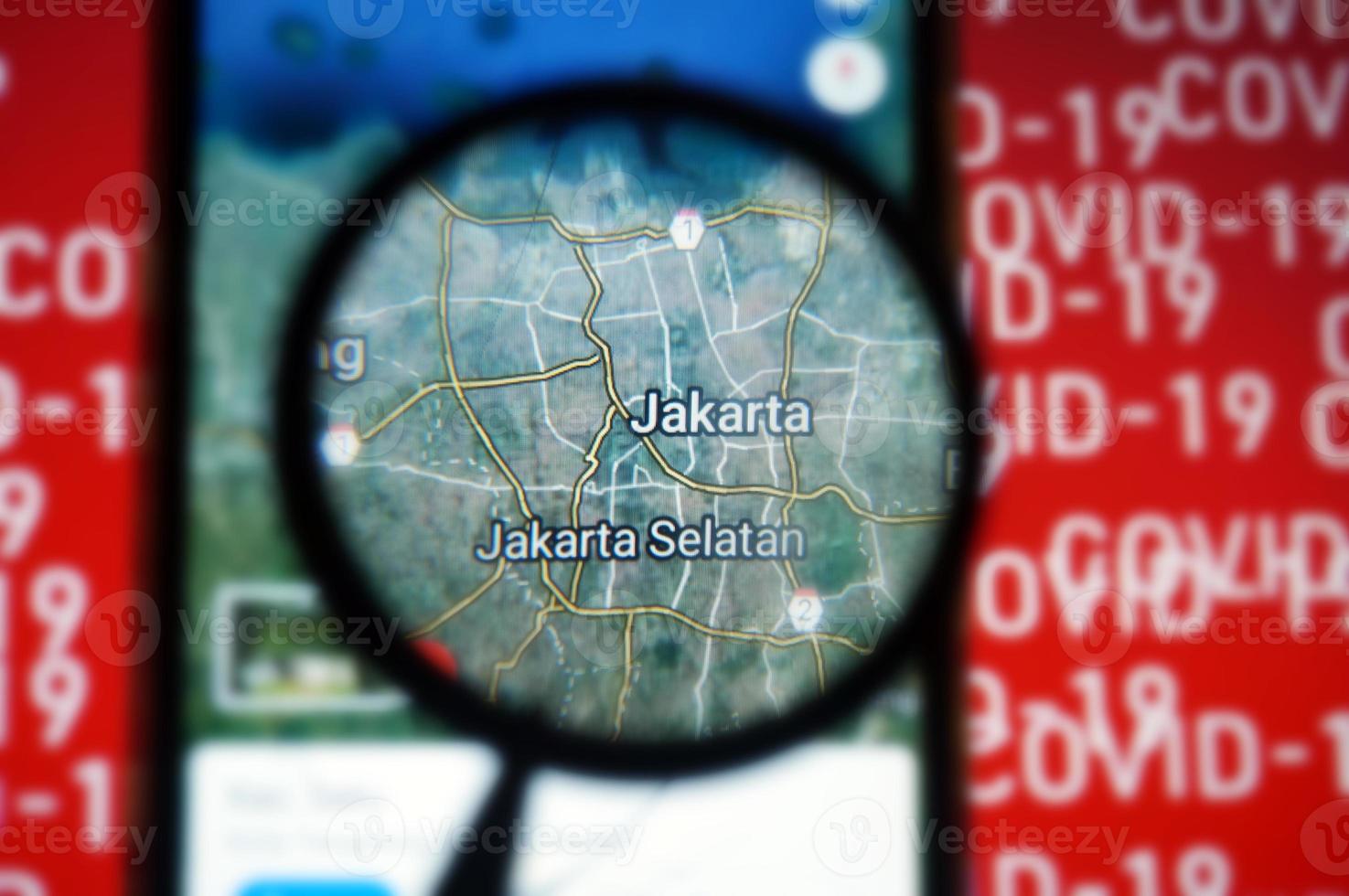Jakarta, Indonesia on google maps under magnifying glass with Red Covid-19 text Background. photo