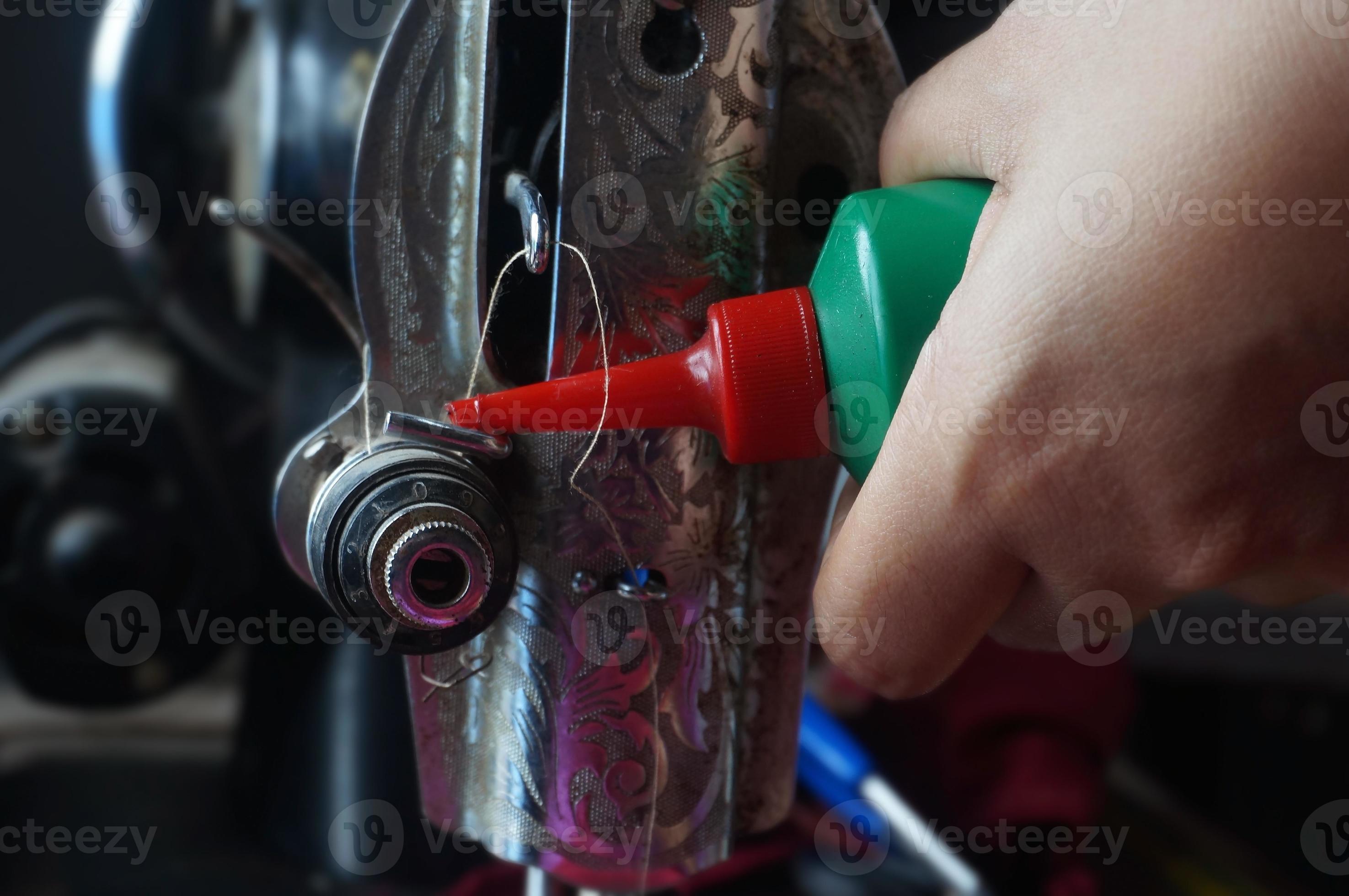 Hand holding sewing machine oil bottle. Oiling parts of sewing machine
