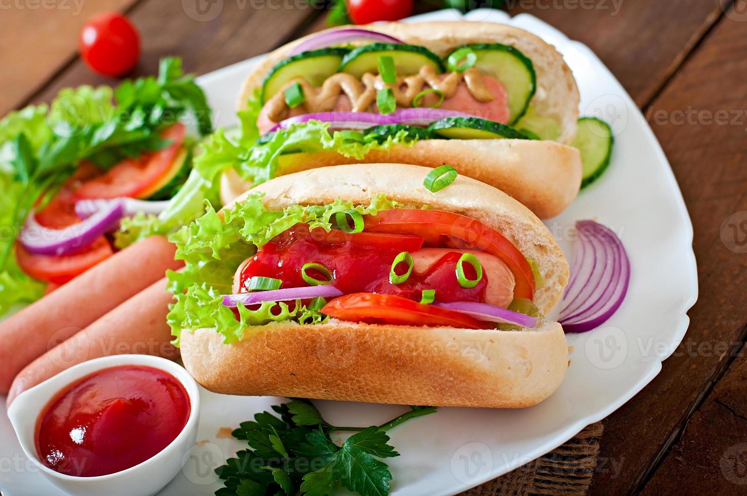 Hotdog with ketchup, mustard, lettuce and vegetables on wooden table photo