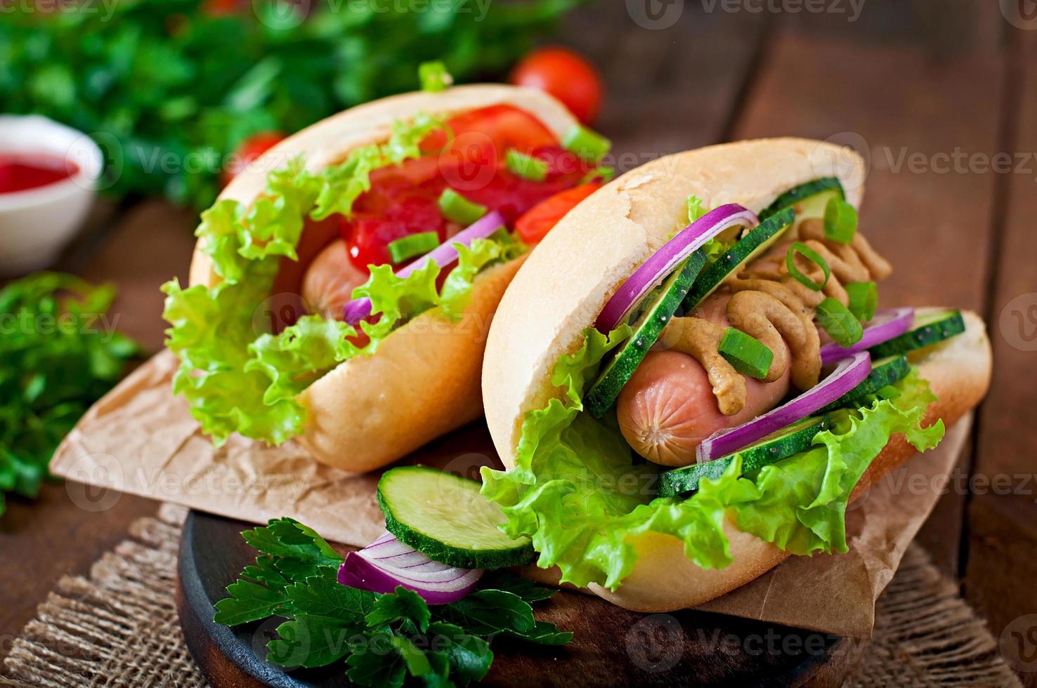 Hot Dog con salsa de tomate, mostaza, lechuga y verduras en la mesa de madera foto