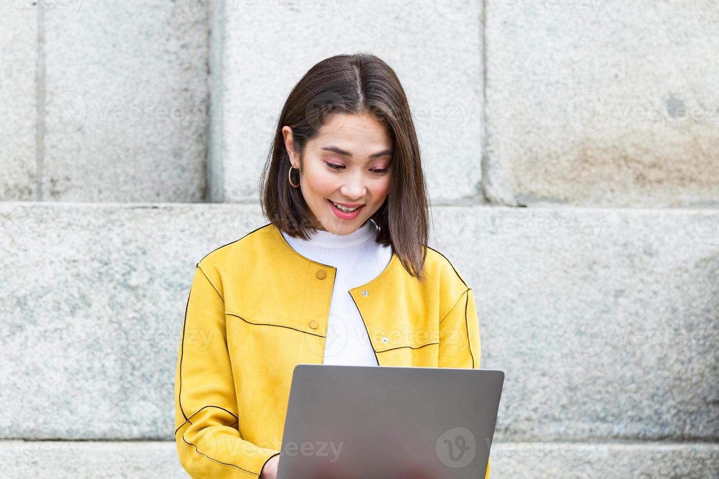 Beautiful asian woman using laptop computer. Smiling asian girl sitting on stairs and using a laptop. Asian business woman using laptop computer photo