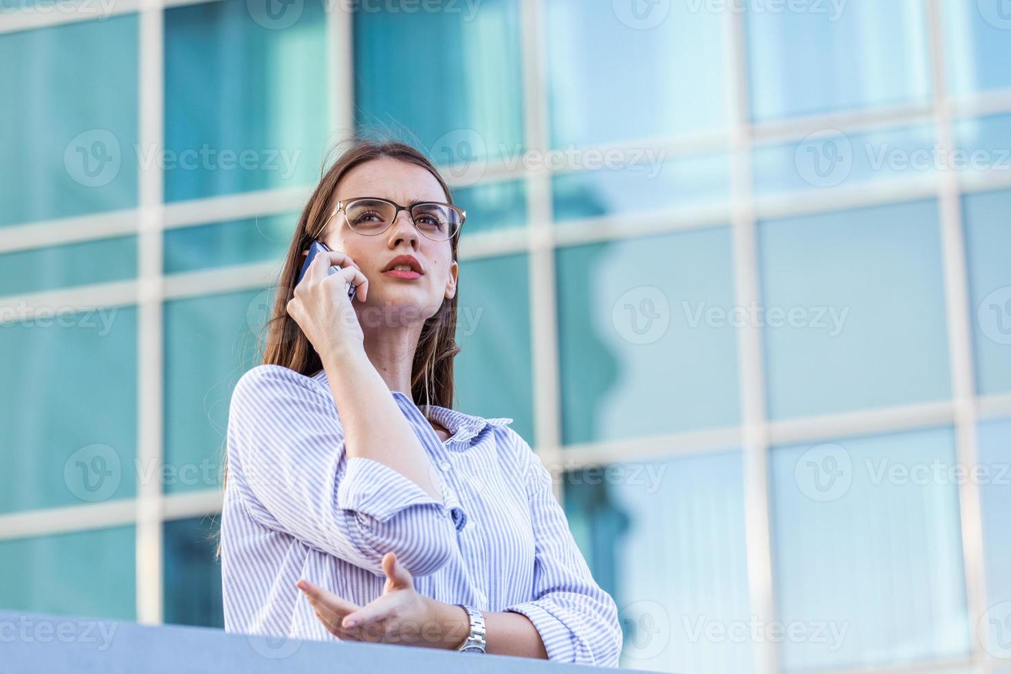 Smart successful business woman, financial representative, legal attorney, consultant, modern professional talking on mobile phone in front of windows in an office building photo