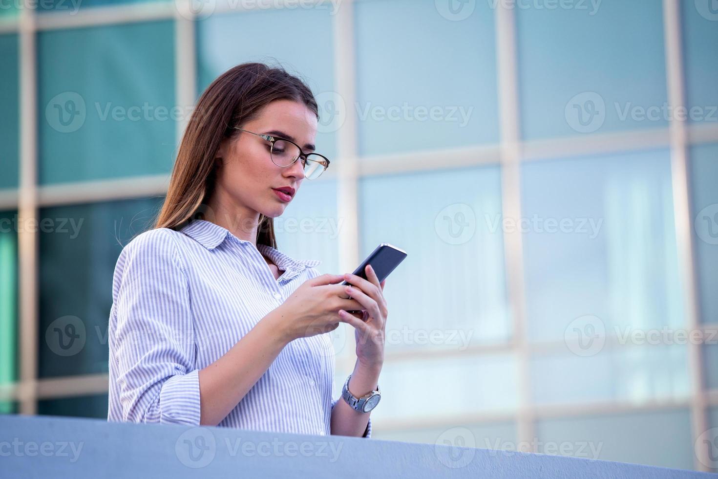 Executive business woman looking at mobile smartphone in the street with office buildings in the background photo