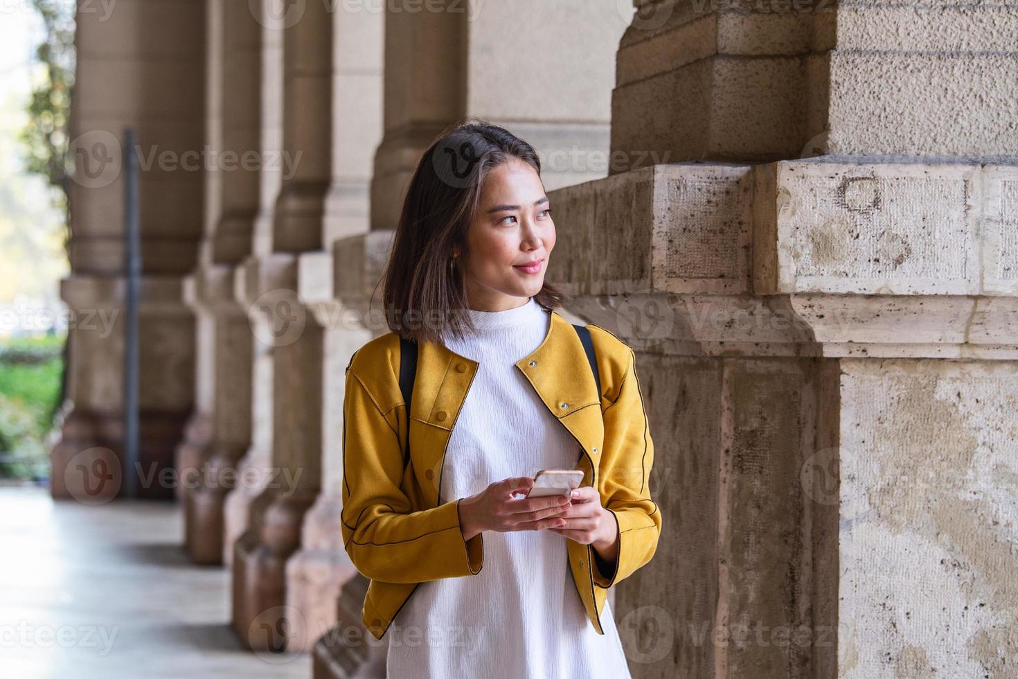 Beautiful asian woman using an application to send an sms message in her smartphone device. Happy young Asian woman with smartphone standing in the street photo