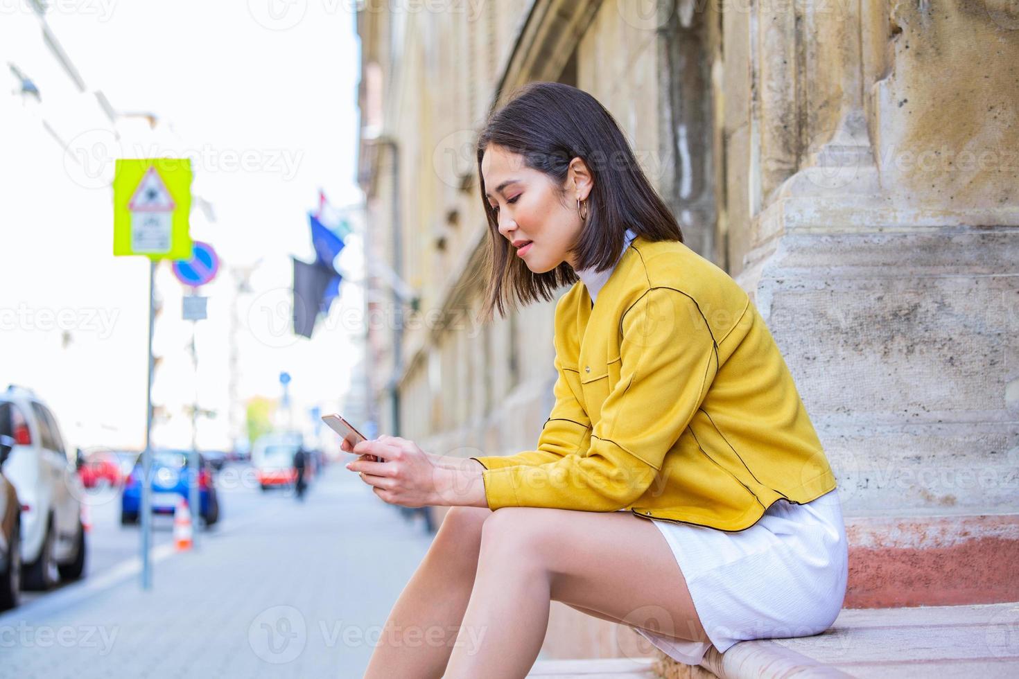 Smiling asian woman working on mobile smart phone while sitting on the floor Asian woman talking on mobile cellphone texting and surfing the net photo