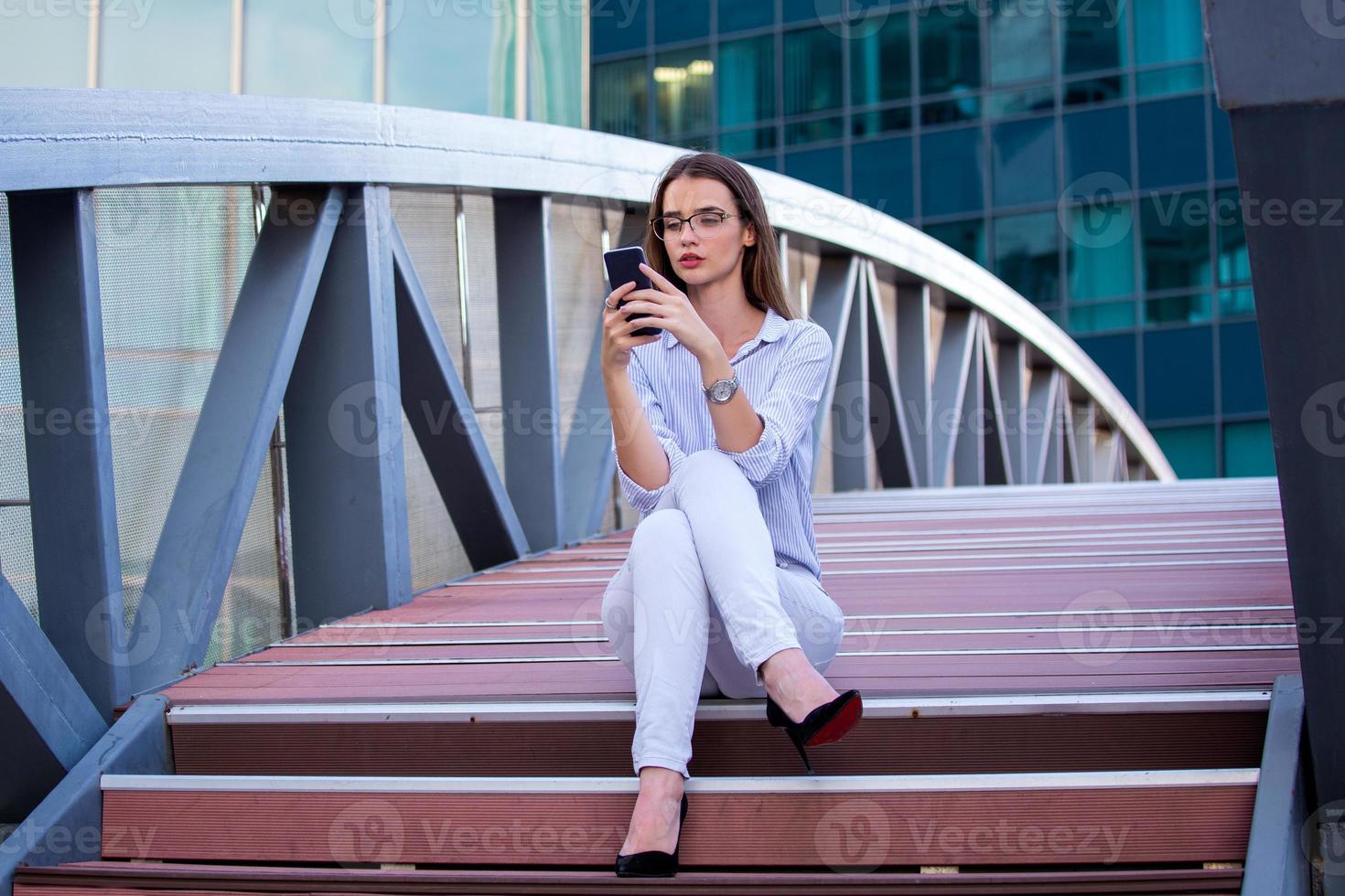 Executive business woman looking at mobile smartphone in the street with office buildings in the background photo