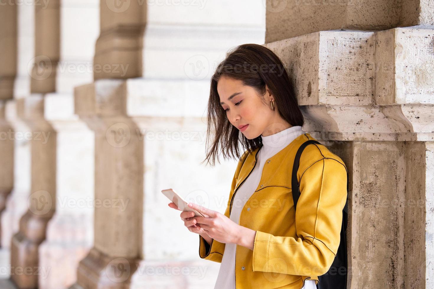 Beautiful asian woman using an application to send an sms message in her smartphone device. Happy young Asian woman with smartphone standing in the street photo