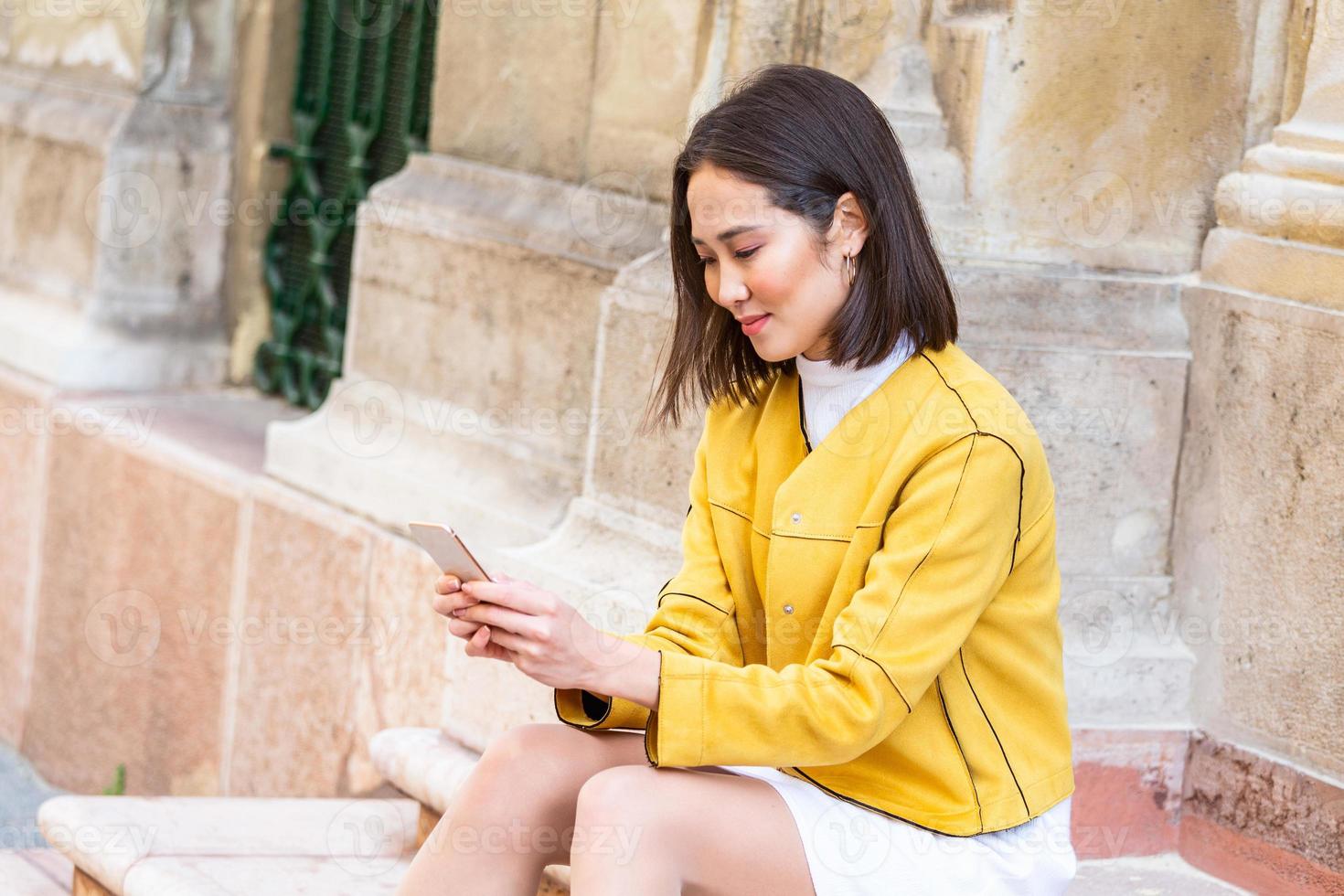 Smiling asian woman working on mobile smart phone while sitting on the floor Asian woman talking on mobile cellphone texting and surfing the net photo