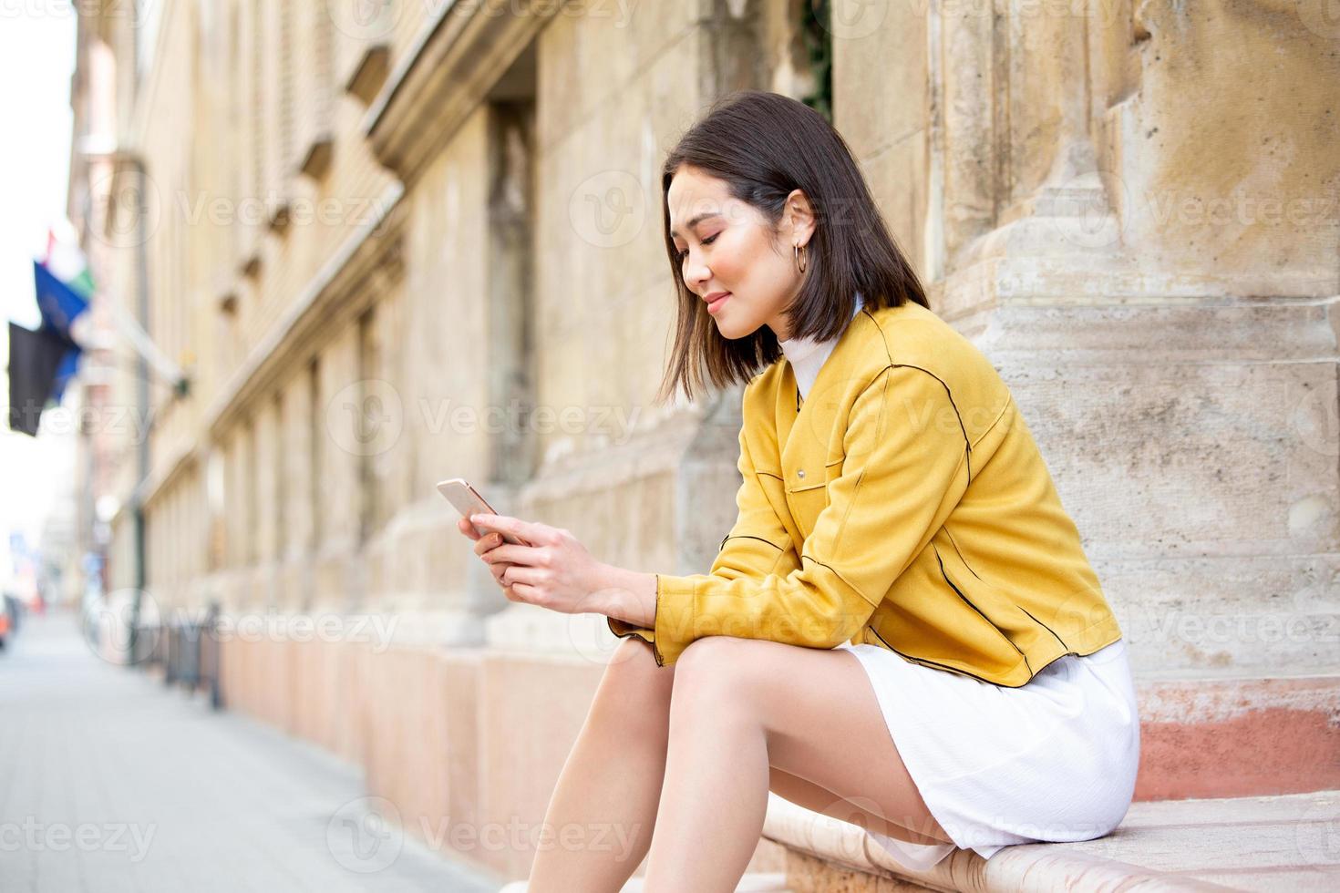 Smiling asian woman working on mobile smart phone while sitting on the floor Asian woman talking on mobile cellphone texting and surfing the net photo