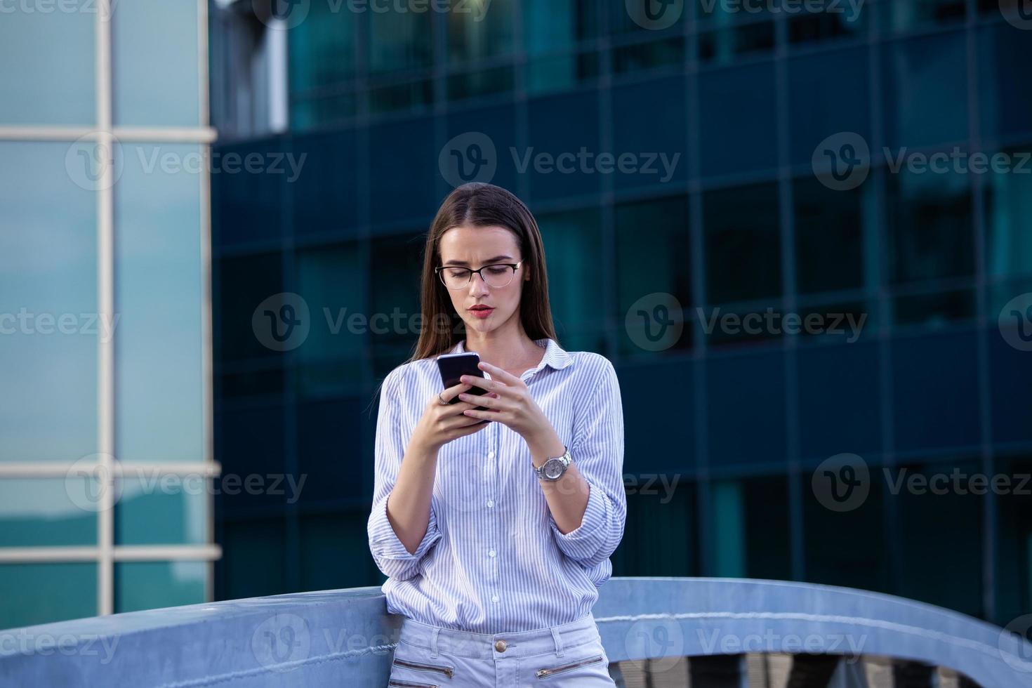 Executive business woman looking at mobile smartphone in the street with office buildings in the background photo