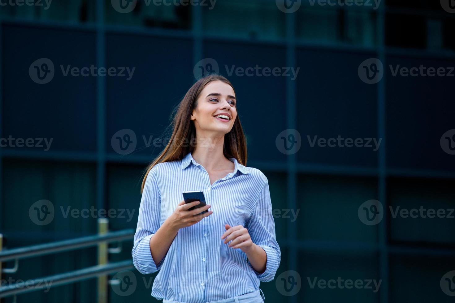 Happy smiling business woman talking on mobile smartphone in the street with office buildings in the background photo