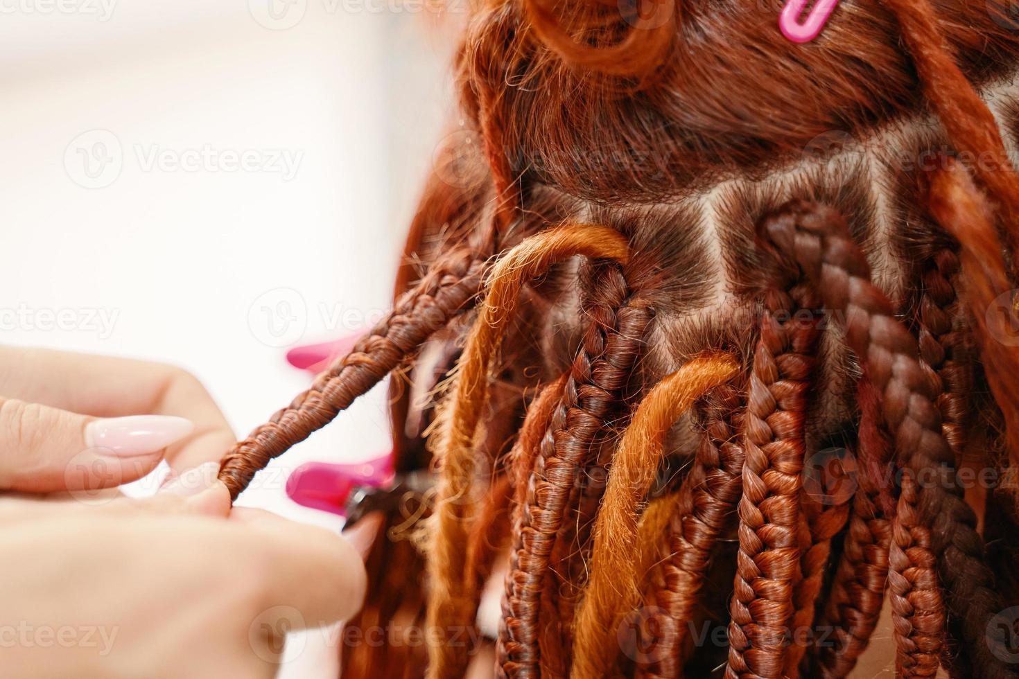 manos de peluquero trenzan rastas de jengibre de niña. foto