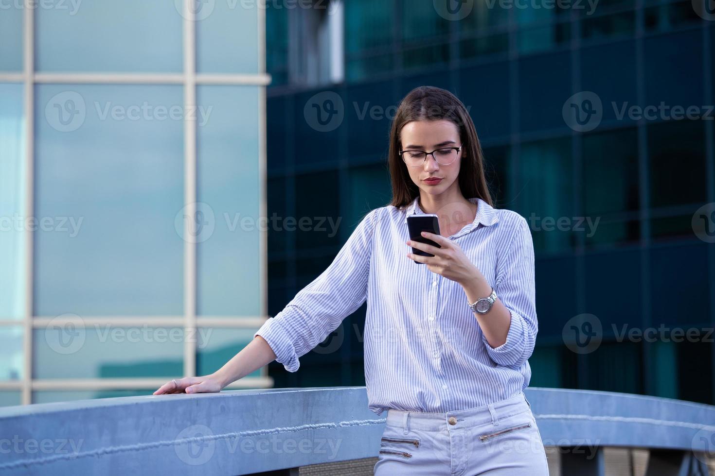 Executive business woman looking at mobile smartphone in the street with office buildings in the background photo