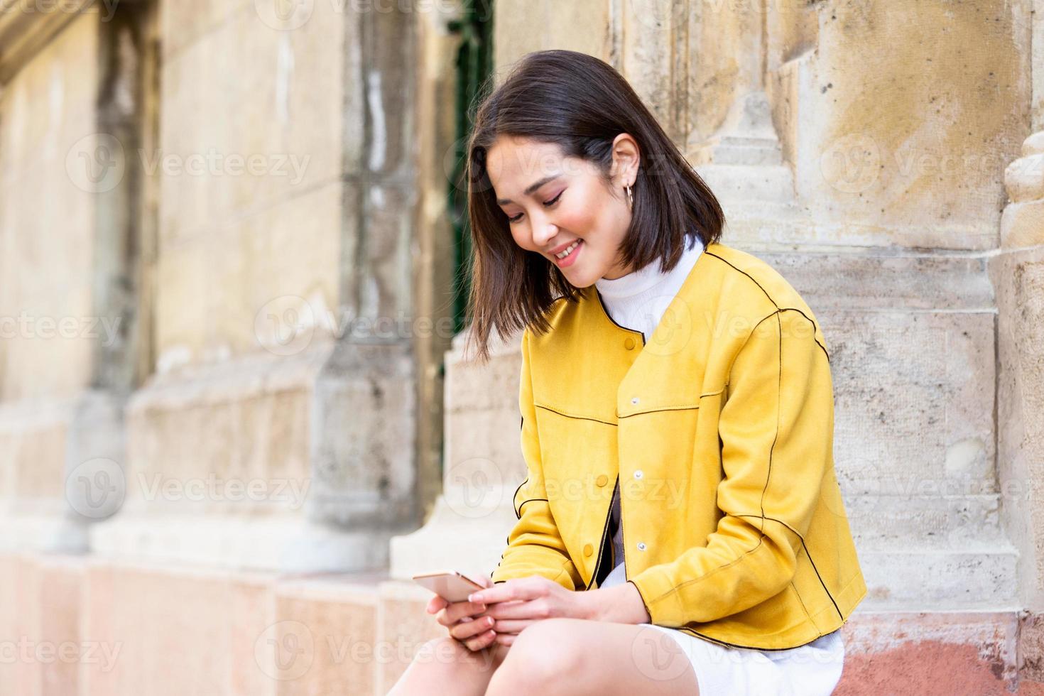 Smiling asian woman working on mobile smart phone while sitting on the floor Asian woman talking on mobile cellphone texting and surfing the net photo