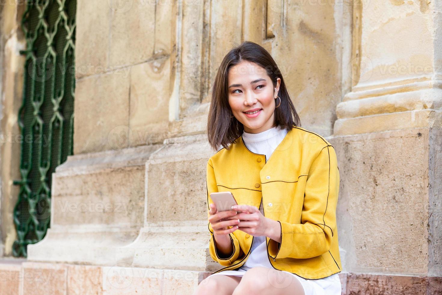 Smiling asian woman working on mobile smart phone while sitting on the floor Asian woman talking on mobile cellphone texting and surfing the net photo