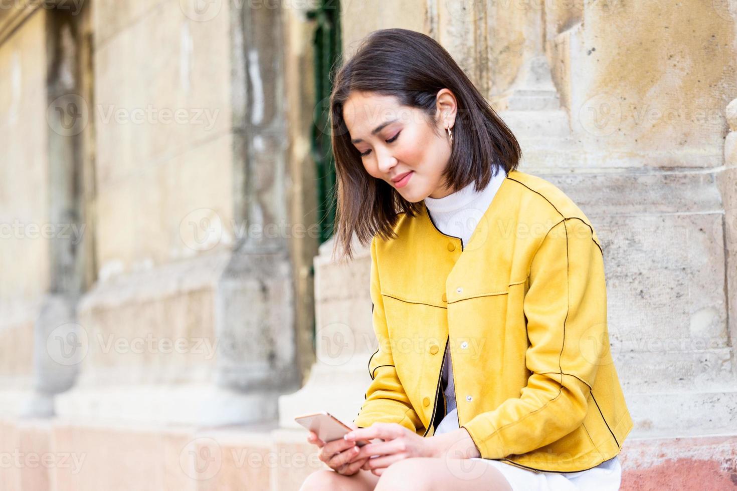 Smiling asian woman working on mobile smart phone while sitting on the floor Asian woman talking on mobile cellphone texting and surfing the net photo