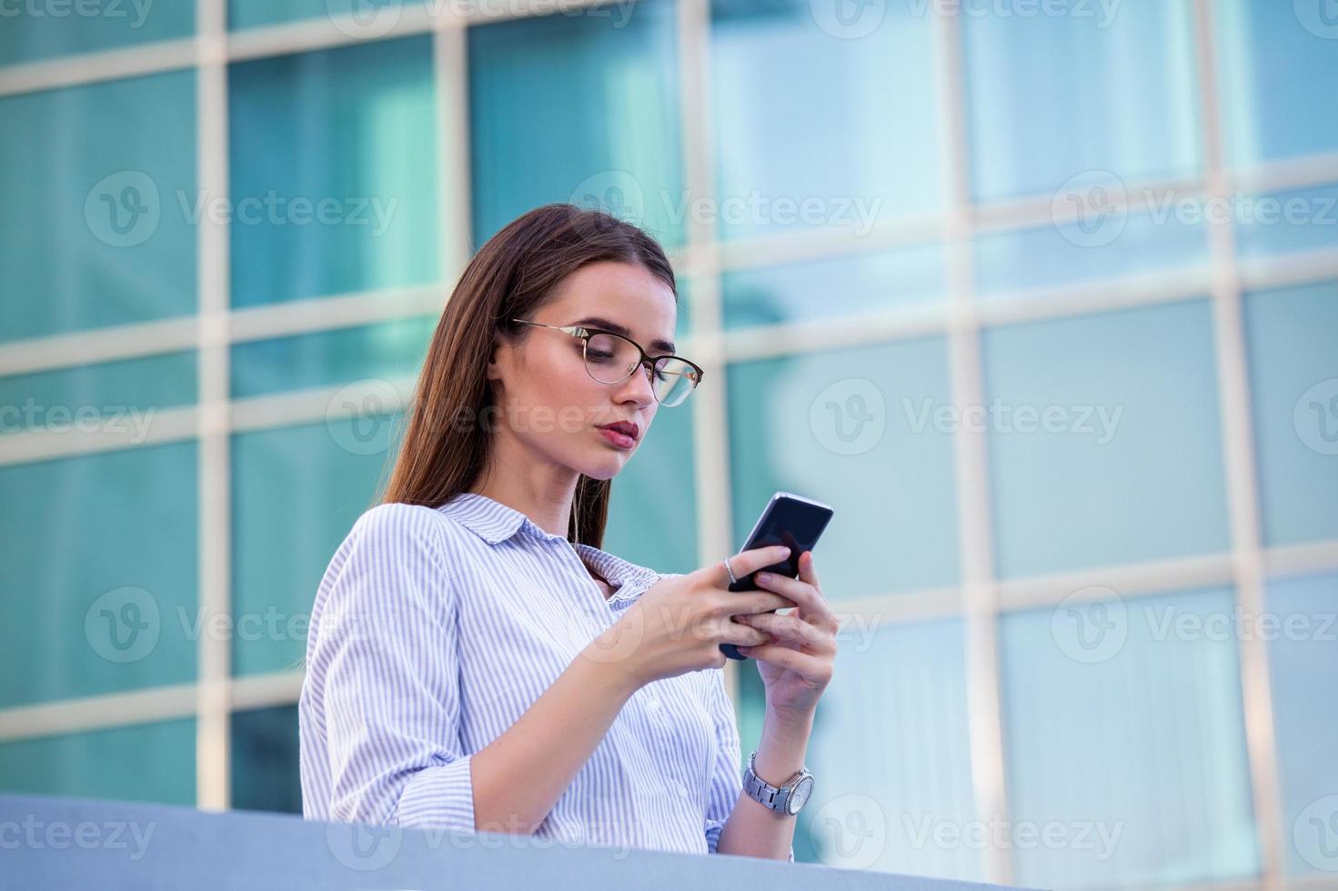 Executive business woman looking at mobile smartphone in the street with office buildings in the background photo