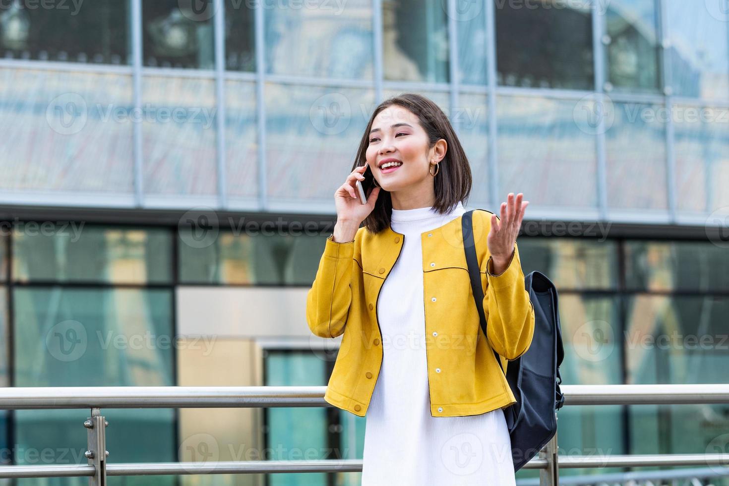 Happy smiling business woman talking on mobile smartphone in the street with office buildings in the background. Executive business Asian woman talking on mobile cellphone photo