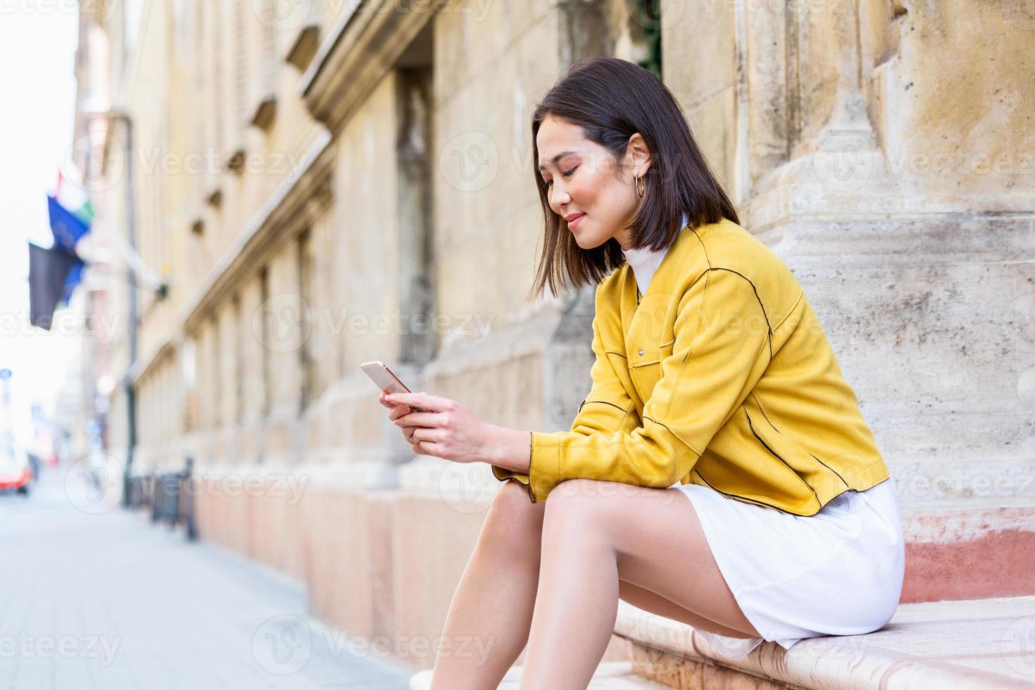 Smiling asian woman working on mobile smart phone while sitting on the floor Asian woman talking on mobile cellphone texting and surfing the net photo