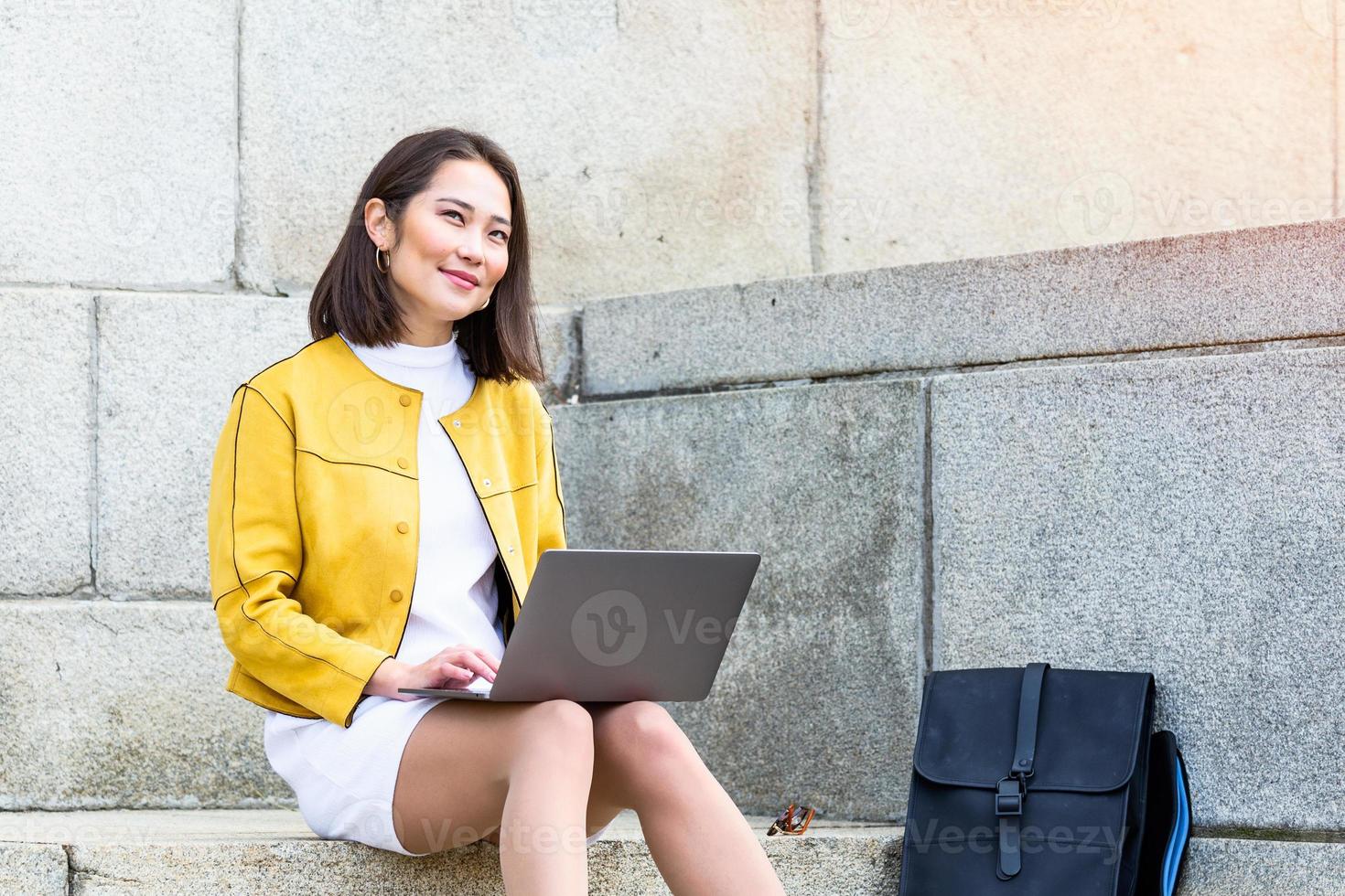 Beautiful asian woman using laptop computer. Smiling asian girl sitting on stairs and using a laptop. Asian business woman using laptop computer photo