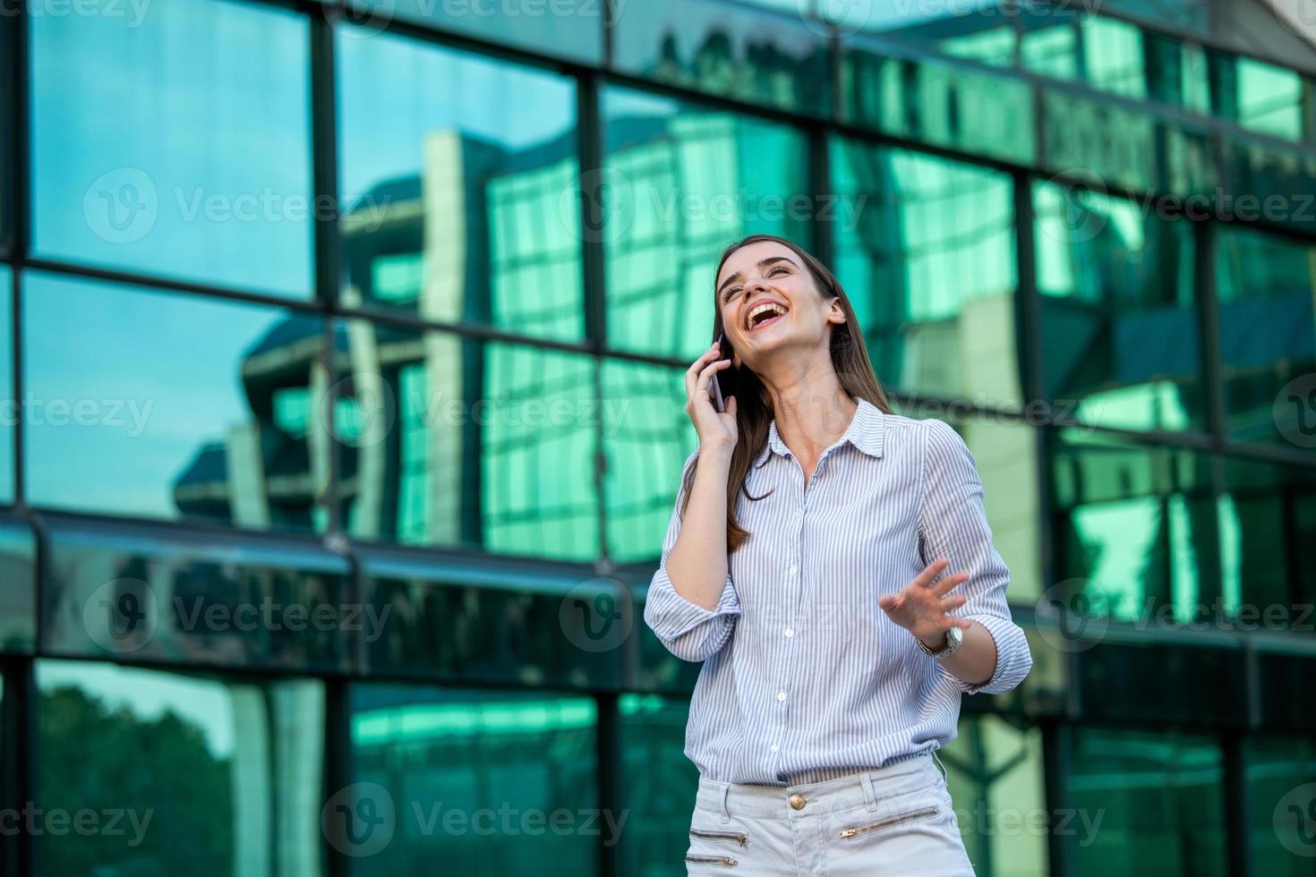 Executive business woman talking on mobile smartphone in the street with office buildings in the background. Young woman with smartphone standing against street blurred building background. photo