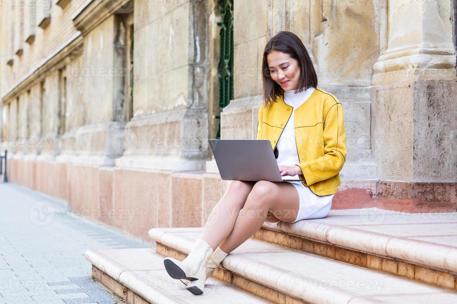 Beautiful asian woman using laptop computer. Smiling asian girl sitting on stairs and using a laptop. Asian business woman using laptop computer photo