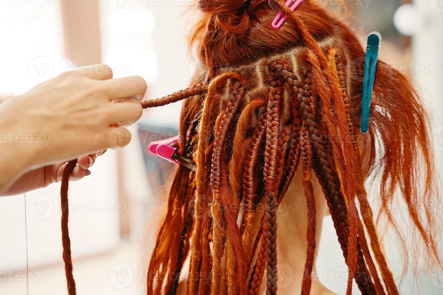 manos de peluquero trenzan rastas de jengibre de niña. foto