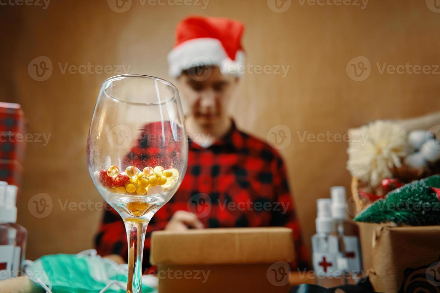 Glass with vitamins in close-up and man in Santa hat in background. photo