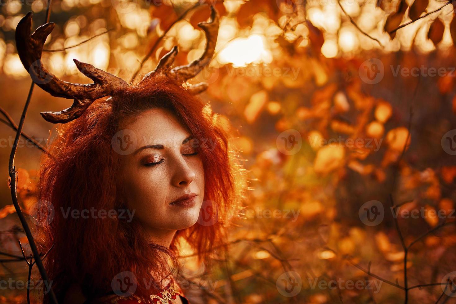 Woman in long red dress with deer horns in autumn forest. photo