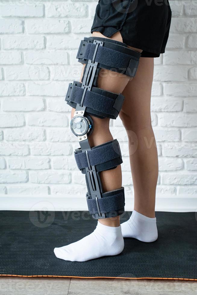 Female wearing knee orthosis or knee support brace after surgery on leg photo