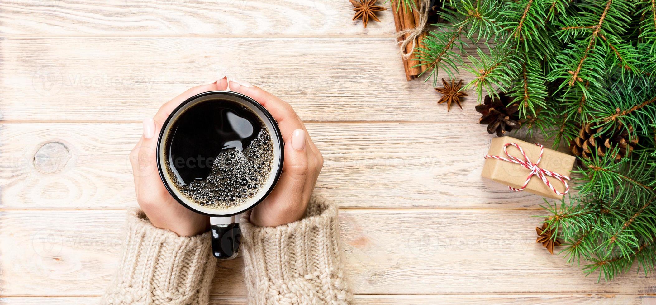 female hands holding coffee cupon wooden table with chrisstmas decoration. Top view banner with copy space photo