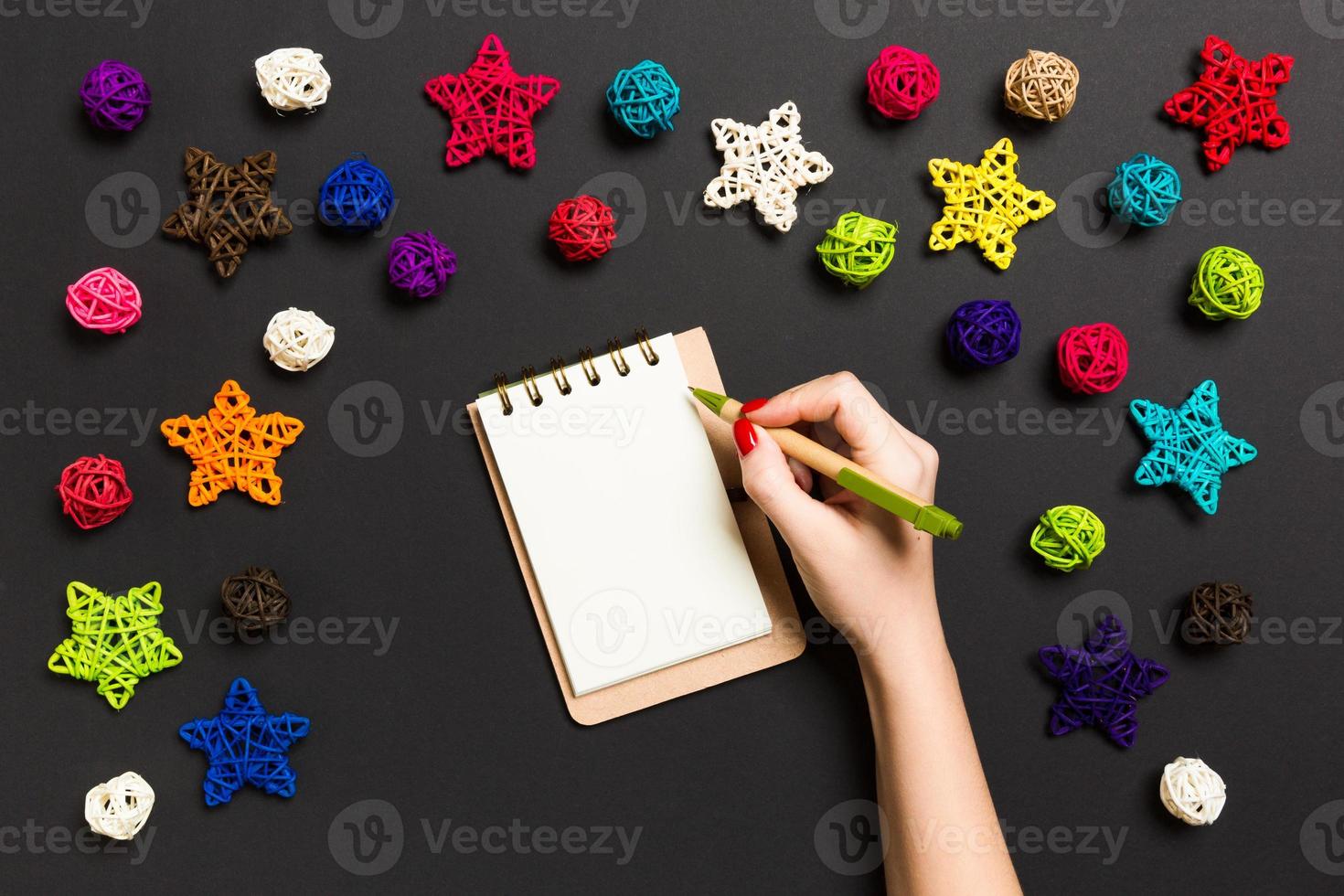 Top view of female hand making some notes in noteebok on colorful background. New Year decorations and toys. Christmas time concept photo