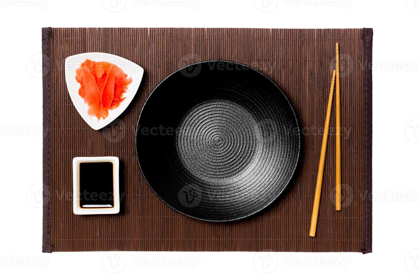 Empty round black plate with chopsticks for sushi, ginger and soy sauce on dark bamboo mat background. Top view with copy space for you design photo