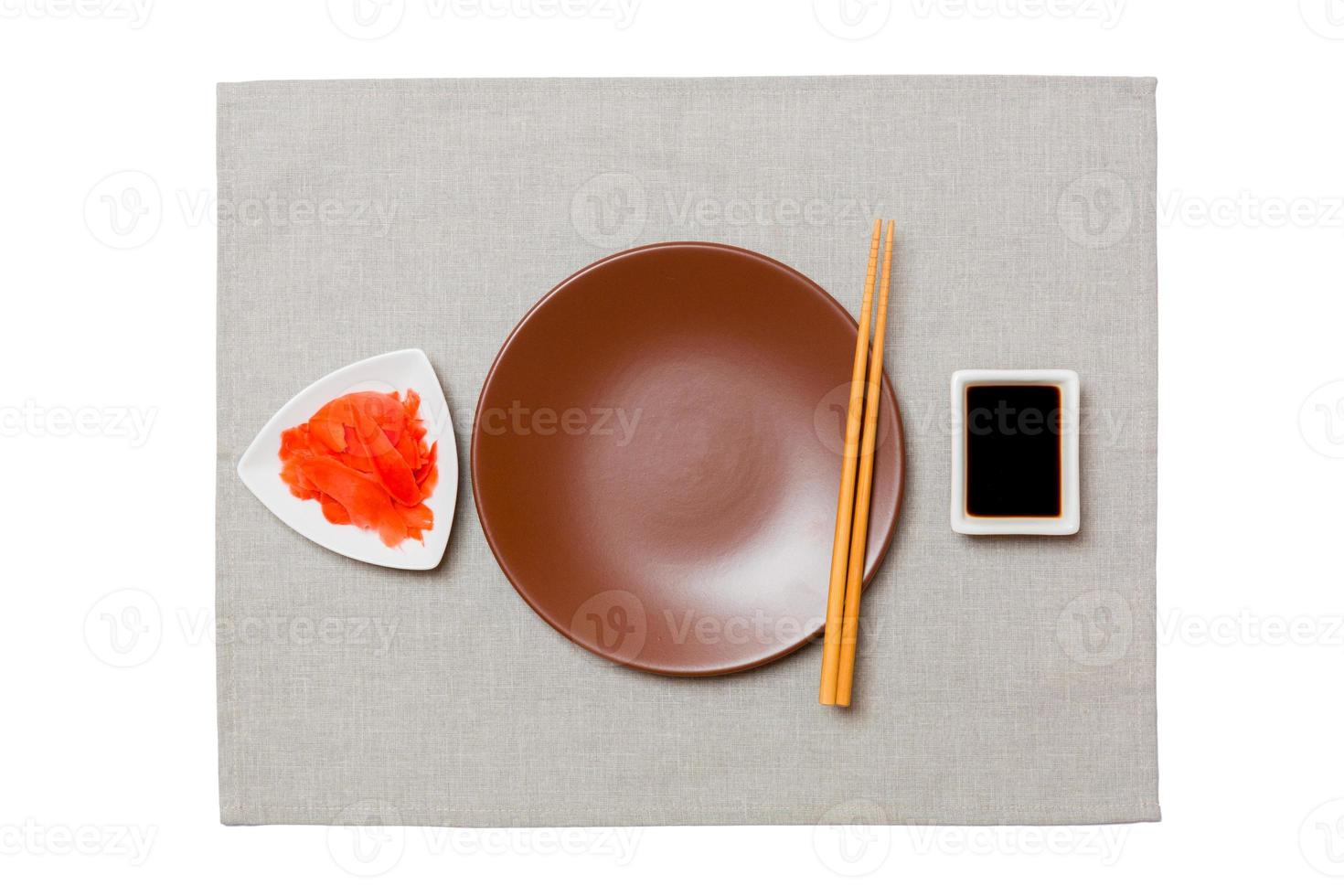 plato marrón redondo vacío con palillos para sushi, jengibre y salsa de soja sobre fondo de servilleta gris. vista superior con espacio de copia para su diseño foto