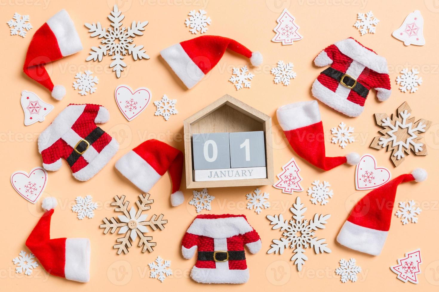 Top view of wooden calendar with Christmas decorations and Santa hats on orange background. The first of January. Happy holiday concept photo