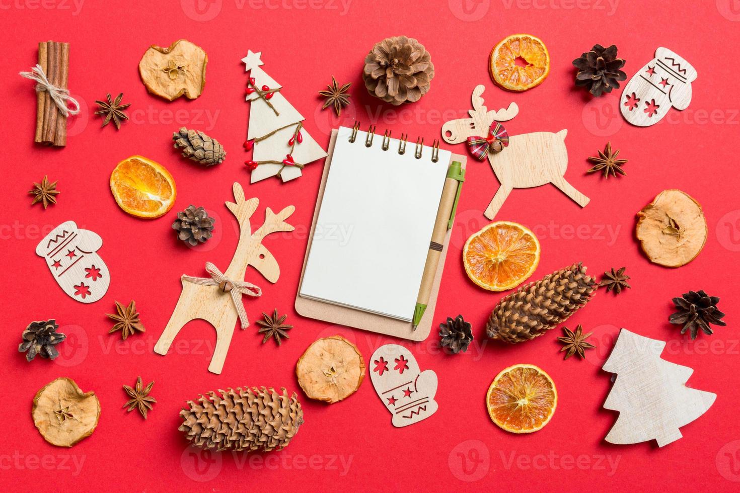 Top view of notebook, red background decorated with festive toys and Christmas symbols reindeers and New Year trees. Holiday concept photo