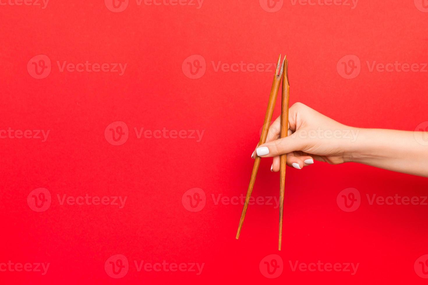 Wooden chopsticks holded with female hands on red background. Ready for eating concepts with empty space photo