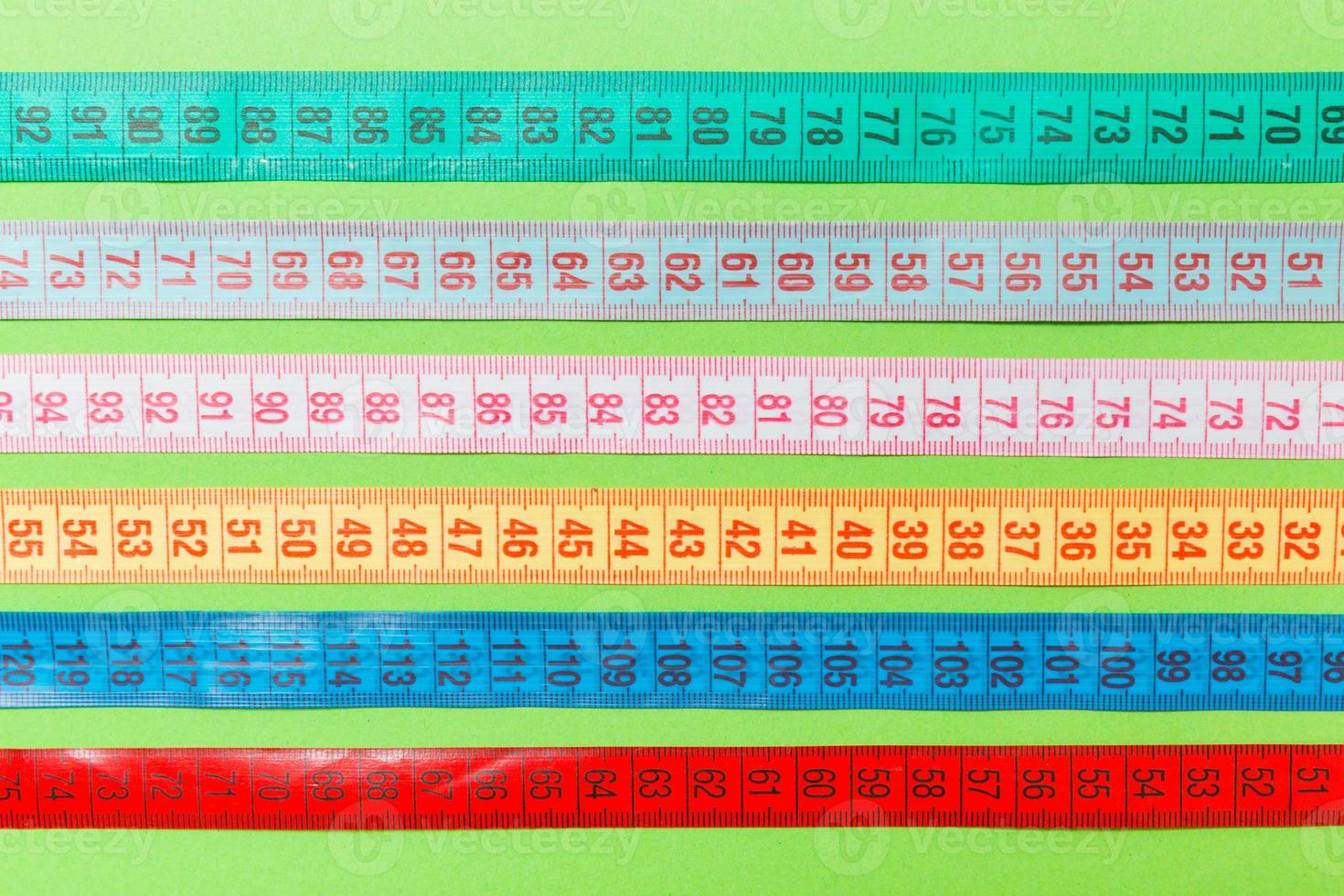 Close up of a group of colorful measure tapes lying in rows as a background. Diet concept on green background photo